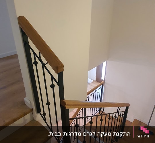 מעקה ברזל עם ידית עץ במדרגות עץ